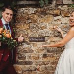 Smiling couple pointing at sign on brick wall.