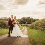 Couple in wedding attire on countryside road.