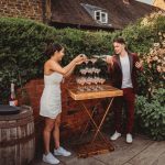 Couple pouring champagne into glass tower outdoors.