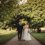 Bride and groom walking on tree-lined path.