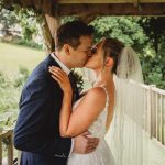 Newlyweds kissing under wooden pergola in garden