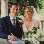 Bride and groom signing wedding certificate outdoors.