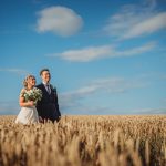 Bride and groom in wheat field under blue sky.