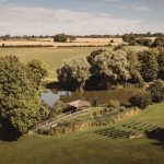 Countryside view with pond and trees, fields beyond.