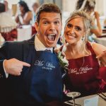 Smiling couple wearing personalised aprons at wedding reception.