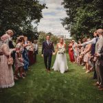 Bride and groom walk through confetti aisle outdoors.