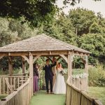 Happy couple marries under a wooden gazebo.