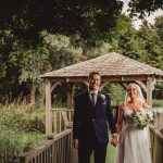 Bride and groom smiling near garden gazebo.