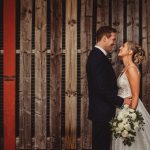 Bride and groom smiling in front of wooden wall.