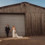 Bride and groom holding hands by barn door.