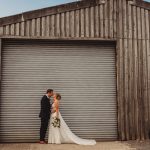 Bride and groom kiss outside industrial building.