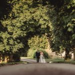 Wedding couple walking under tree-lined path.