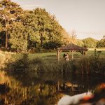 Couple in gazebo by scenic pond and trees.