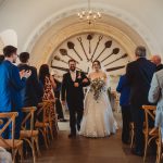 Bride and groom walking down the aisle, guests clapping.