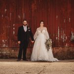 Bride and groom holding hands outside rustic barn.