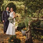 Wedding couple in garden, autumn leaves, stone statue.