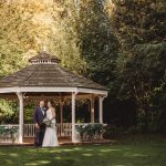 Wedding couple in garden gazebo surrounded by trees.