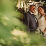 Bride and groom posing among greenery, wedding day.