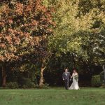 Couple walking in lush garden, wedding attire.