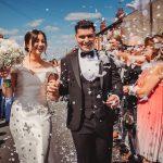 Newlywed couple smiling with wedding guests and confetti.