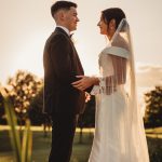 Bride and groom at sunset, holding hands outdoors.