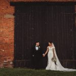 Bride and groom holding hands by brick wall.