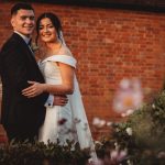 Bride and groom smiling outside brick building.