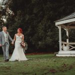 Couple walking hand-in-hand, bride in white gown.