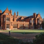 Victorian manor house with gardens and clear sky.