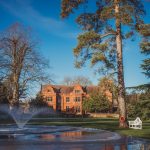 Historic manor house by pond and fountain in garden.