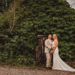 Wedding couple smiling by overgrown wooden door.