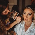 Makeup artist applying eyeshadow to woman in robe.