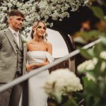 Bride and groom standing under floral archway.