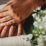 Bride and groom hands with wedding rings and flowers.