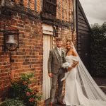 Bride and groom by rustic brick building.