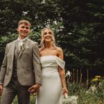 Smiling couple in wedding attire outdoors.