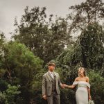 Bride and groom holding hands in lush garden.