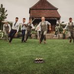 Groomsmen racing towards a tray of drinks on lawn.