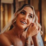 Bride smiling while adjusting earring, tattoo visible