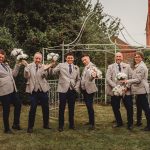 Groomsmen posing with bouquets at outdoor wedding