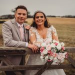 Bride and groom smile by wooden fence