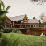 Modern wooden lodge by serene pond and greenery.