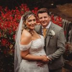 Bride and groom by red flowers and waterfall.