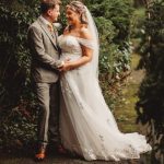 Bride and groom standing together outdoors, smiling.