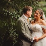 Bride and groom smiling in lush garden setting.