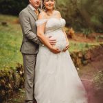 Pregnant bride with groom in garden setting.