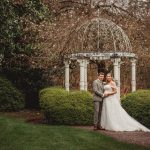 Bride and groom in garden under ornate gazebo.