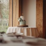 Wedding cake on a decorated table by window.