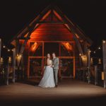 Couple posing outside wooden venue at night.