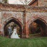 Bride and groom under historic brick arches.